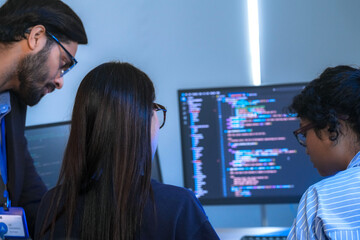 A manager leads a team meeting in a modern office, pointing to the computer screen to explain a project. The diverse group of colleagues works together to find a solution.