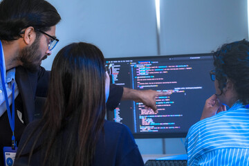 A manager leads a team meeting in a modern office, pointing to the computer screen to explain a project. The diverse group of colleagues works together to find a solution.