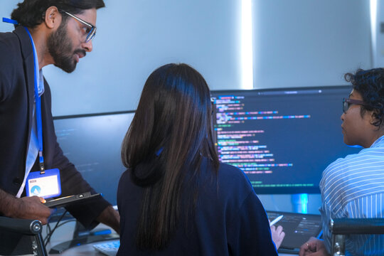 A manager leads a team meeting in a modern office, pointing to the computer screen to explain a project. The diverse group of colleagues works together to find a solution.