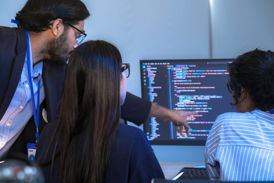 An AI development team collaborates on a project. A senior machine learning engineer mentors his team, reviewing a neural network's code in a futuristic tech hub. - Powered by Adobe