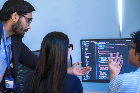 A manager leads a team meeting in a modern office, pointing to the computer screen to explain a project. The diverse group of colleagues works together to find a solution.