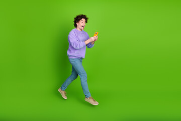 Energetic young male holding a phone with excitement, wearing a purple sweatshirt, standing against...