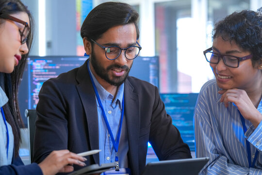 A diverse creative team brainstorms ideas in a meeting, using tablets for collaboration. Smiling professionals discuss a new UI/UX design for an app in a modern office.