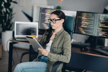 Charming female programmer working on a tablet in a modern office with multiple coding screens in the background.
