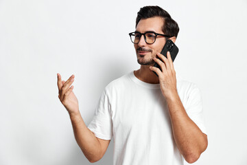 Full body smiling young man talking on mobile phone while gesturing with hand, wearing casual white...