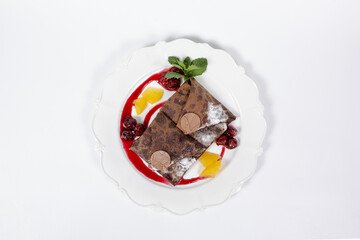 Chocolate pancakes with fruit and chocolate on a white plate, top view on a white background