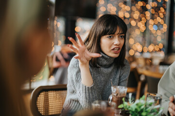 A young woman animatedly discussing something with friends at a cozy cafe with warm lighting. The blurred background enhances the festive and conversational atmosphere.