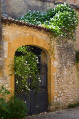 Arched gate surrounded by warm sandstone and flowering plants in France