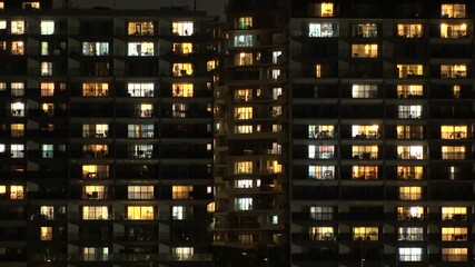 Time lapse shot of illuminated modern high rise residential apartment building with glowing windows in dense urban cityscape at night. Lifestyle and real estate concept. Shot in Tokyo, Japan.