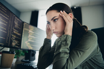 Young female programmer concentrating on coding in a modern workspace with multiple computer...