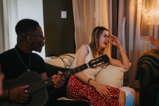 A warm gathering of friends with a man playing guitar and a woman laughing in a comfortable home environment, exuding joy and togetherness.