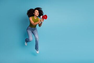 Full of energy, happy young woman with a megaphone leaping against a vibrant blue background