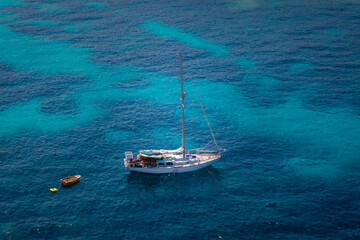 A sailboat anchored in crystal-clear turquoise waters of the Mediterranean Sea. The vibrant shades...
