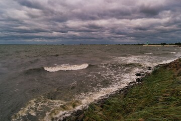 Dark clouds loom over a turbulent sea near a coastal landscape during an overcast day