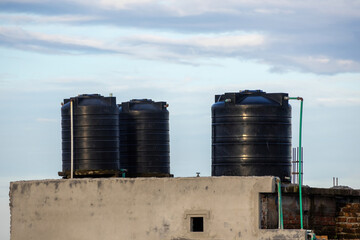Close-up of three black plastic water tanks from a house roof in Bangladesh with a cloudy afternoon...
