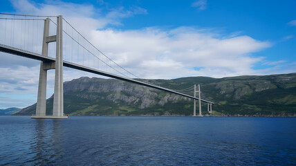 Obraz premium Modern suspension bridge spanning water with dramatic clouds and green hillsides