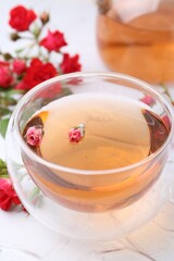 Aromatic tea in glass cup and roses on white table, closeup