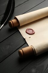 Old rolled scroll and feather on black wooden table, closeup