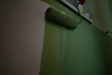 A wall is in the process of being painted green using a roller, highlighting the act of home...