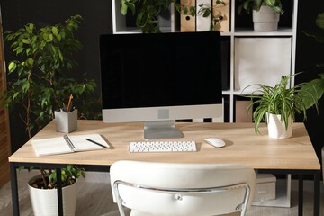Stylish workplace with modern computer, stationery and floral decor in office. Biophilic interior design