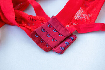 Close-up shot of a red bra hook fastener on a white background. Detailed view of the hook and eye closure on a women's bra strap.