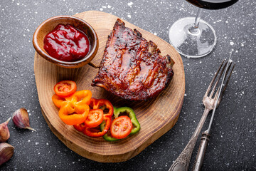 BBQ pork ribs from pork tenderloin with vegetables, cranberry sauce and a glass of red wine on board and dark background top view