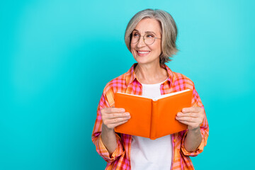 Smiling mature woman reading a book against turquoise background wearing casual checkered shirt and...