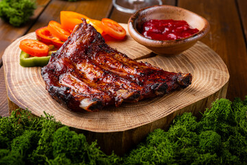 BBQ pork ribs from pork tenderloin with vegetables, cranberry sauce on board and wooden background close up