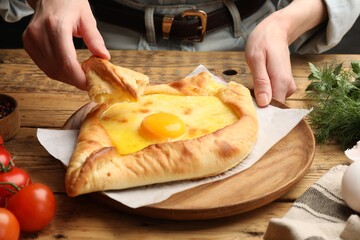 Woman eating delicious khachapuri at wooden table, closeup