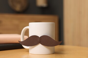 Happy Father's Day. Cup with paper moustache and books on wooden table indoors, closeup