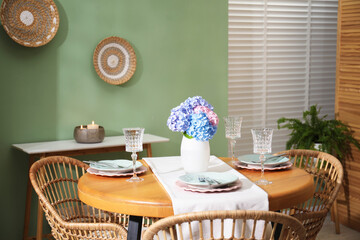 Stylish setting with plates and vase of flowers on wooden table in dining room. Interior design