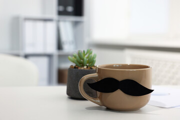Happy Father's Day. Cup with paper moustache on white table indoors, closeup