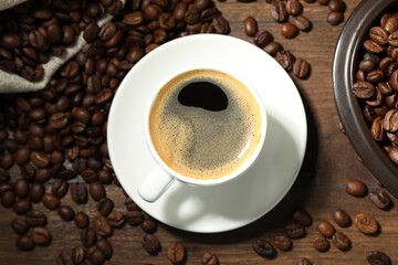 Aromatic coffee in cup and beans on wooden table, flat lay