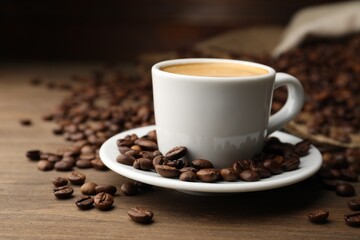 Aromatic coffee in cup and beans on wooden table, closeup