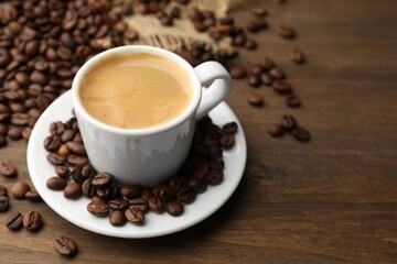 Aromatic coffee in cup and beans on wooden table, closeup. Space for text