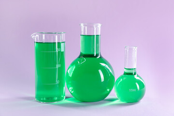 Laboratory glassware with green liquid on lilac background