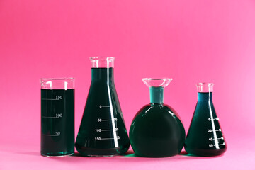 Laboratory glassware with green liquid on pink background. Space for text