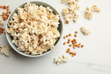 Tasty popcorn and corn kernels on white marble table, flat lay