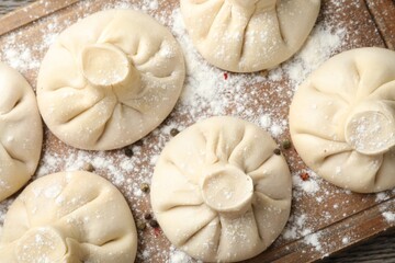 Uncooked khinkalis (dumplings) with peppercorns on wooden board, top view