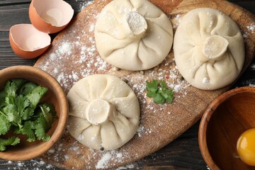 Uncooked khinkalis (dumplings) and ingredients on dark wooden table, flat lay