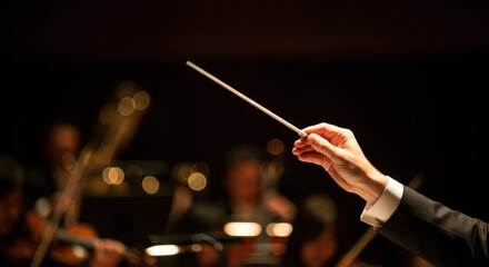 Conductor's hands leading orchestra with baton in lighted concert hall. Hands conducting orchestra include skillful gestures, focused musicians in background creating harmonious sounds.