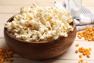 Tasty popcorn and corn kernels on light wooden table, closeup