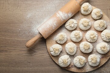 Uncooked khinkalis (dumplings) and rolling pin on wooden table, top view. Space for text