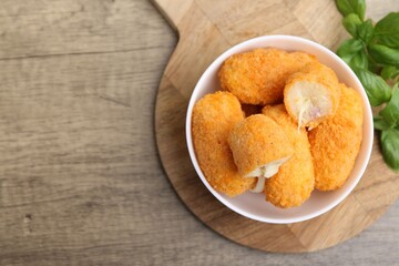 Delicious fried croquettes in bowl and basil on wooden table, flat lay. Space for text
