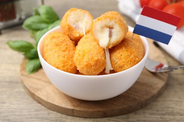 Delicious fried croquettes in bowl and flag of Netherlands on wooden table, closeup