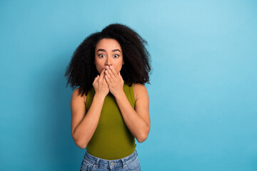 Young woman with surprised expression covering mouth showing astonishment against a solid blue...