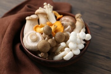 Different raw mushrooms in bowl on wooden table, closeup