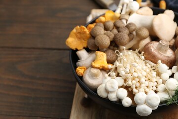 Different raw mushrooms in bowl on wooden table, closeup. Space for text