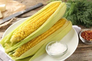 Tasty boiled corncobs, dill and spices on wooden table, closeup