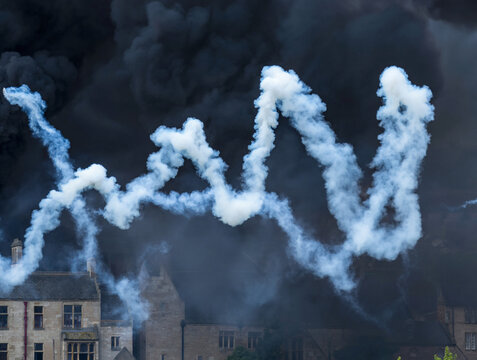 White Smoke Trails Against Dark Sky Above Buildings